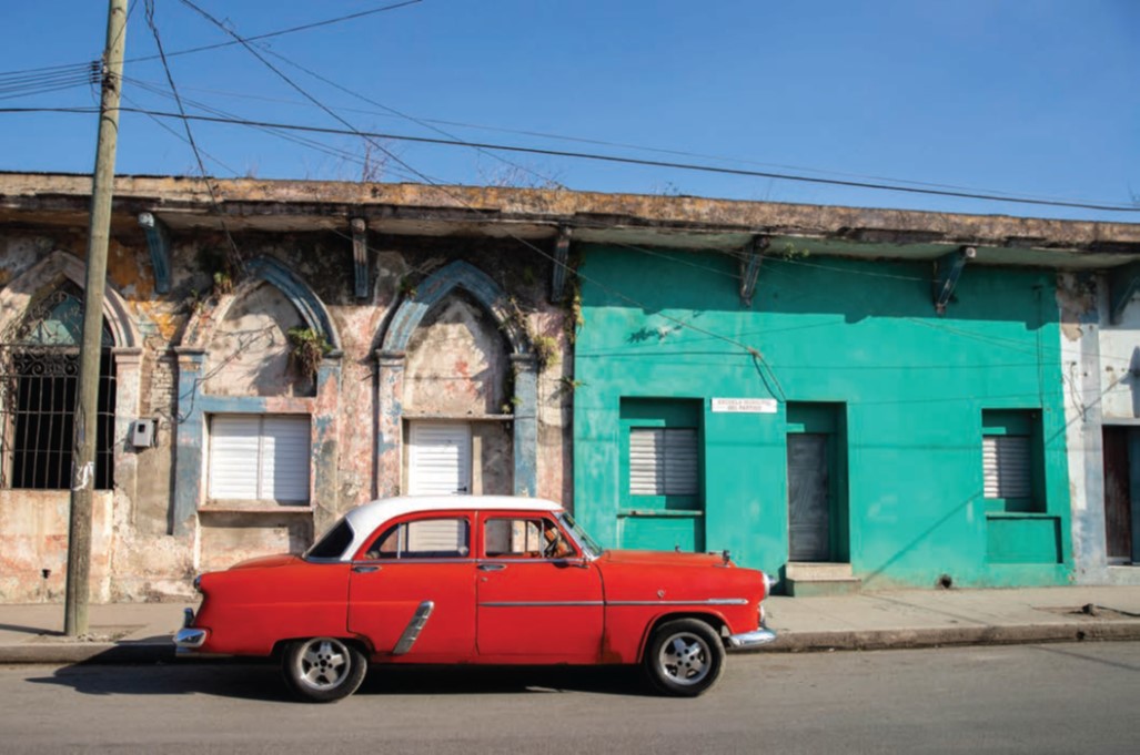 Old red car parked in front of block of residences.